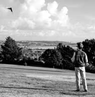 B/W photo: Man flying kite in open expanse of park