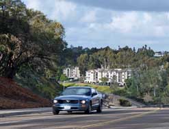 Color photo: Car taking curve at top of hill with apartment blocks in distance