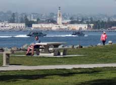 Color photo: Marina Park picnic table with speeding boats and Coronado as backdrop