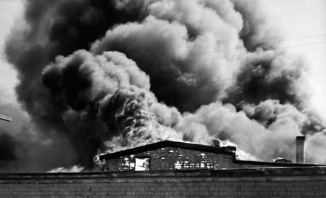 grayscale photograph: building on fire, billowing smoke