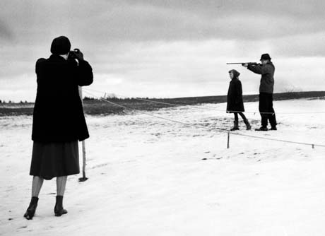 grayscale photograph: Photographer photographs son shooting rifle