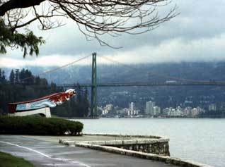Color photo: Stanley Park Seawall Walkway view of totem and Lions Gate Bridge