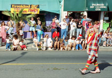 Color photo: Clown in street in front of spectators on sidewalk