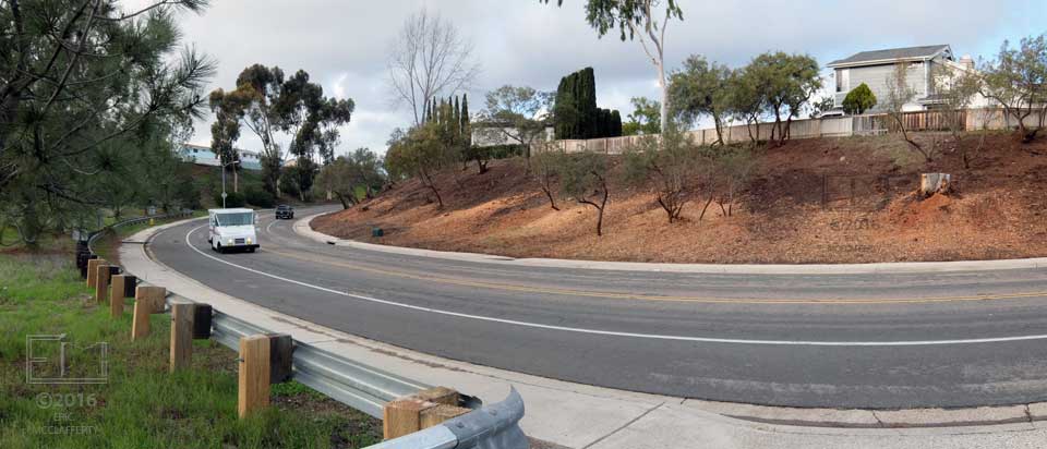 Curve in roadway with rebuilt gaurdrail on near side and brushless/de-vegetated hillside on far side
