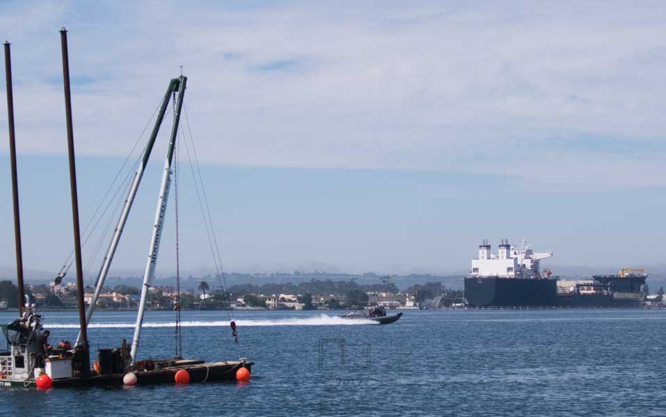 Small boat/large crane vessal passed by speeding boat, large freighter moored on oppisite shore