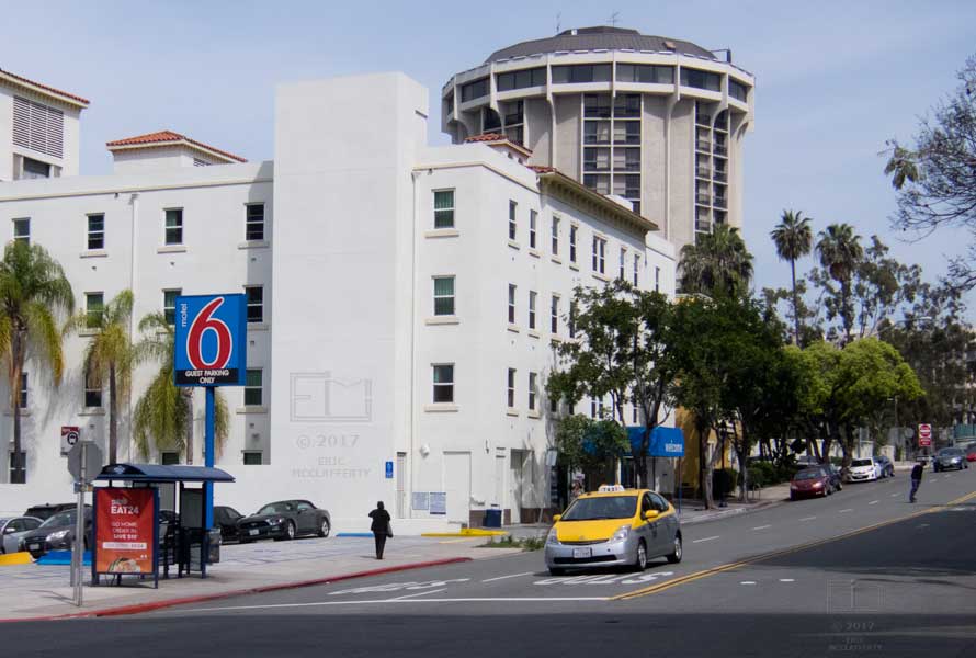 Street view of Motel 6 with taxi and skateboarder coming down street
