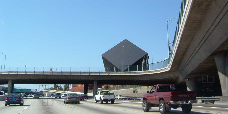 View from freeway of an apparent square, black building tilted ~45 degrees on its corner