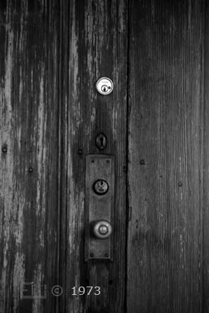 B/W photo: Timeworn door with new, vintage, and antique locks - Embedded text: 1973