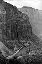 B/W photo:  Telephoto, portrait view of switch backed roadway, cliffs, and 'West Temple' in distance