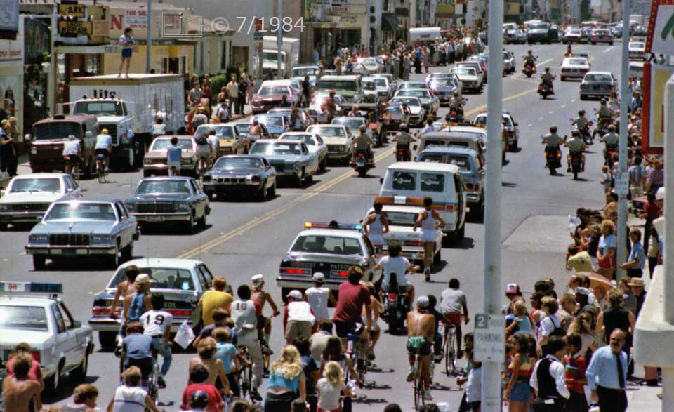 Color photo: Telephoto view of passed by motercade and bicyclist entourage - Embedded text: 7/1984