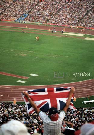 Color photo: Standing spectator, with outstreached arms raised, displays a Union Jack flag  - Embedded text: 8/10/84