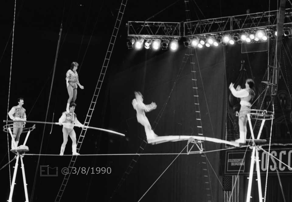 B/W photo: Column of 2 performers on tightrope, one atop the other, while third performer is catapulted  on top of them - Embedded text: 3/8/1990
