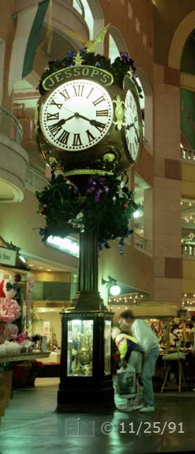 Color photo: Shoppers viewing glass encased mechanism of giant JESSOP'S clock - Embedded text: 11/25/91