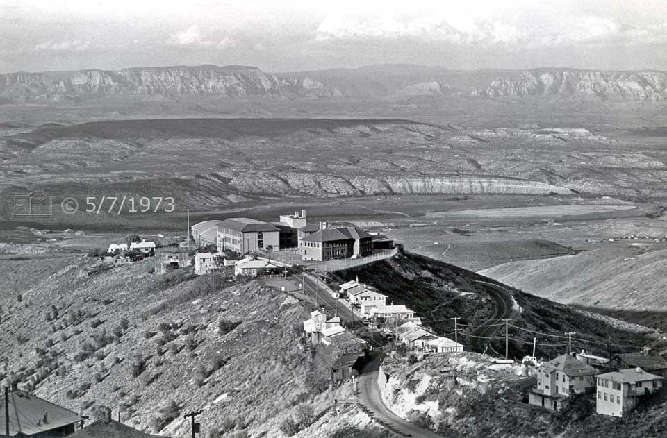 B/W photo: Elevated view of group of buildings at end of a road with valley, hills and mountains as backdrop - Embedded text: 5/7/1973