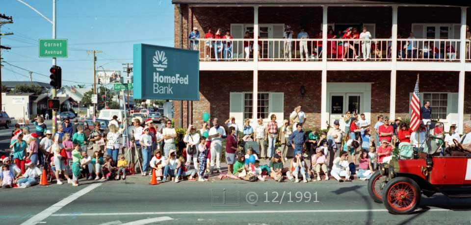 Color photo: Antique red automobile in front of curbside and balcony spectators of HomeFed Bank - Embedded text: 12/1991