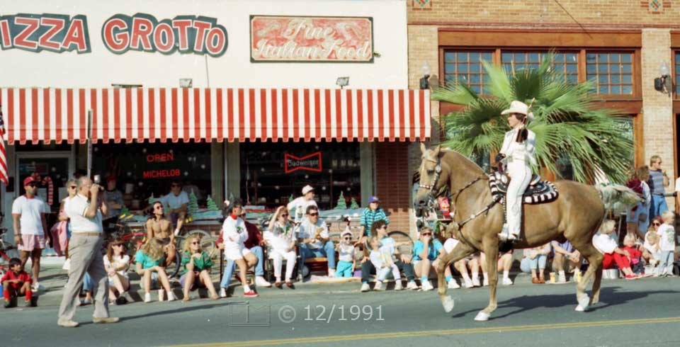 Color  photo: Man on horse being photographed by photographer in street - Embedded text: 12/1991