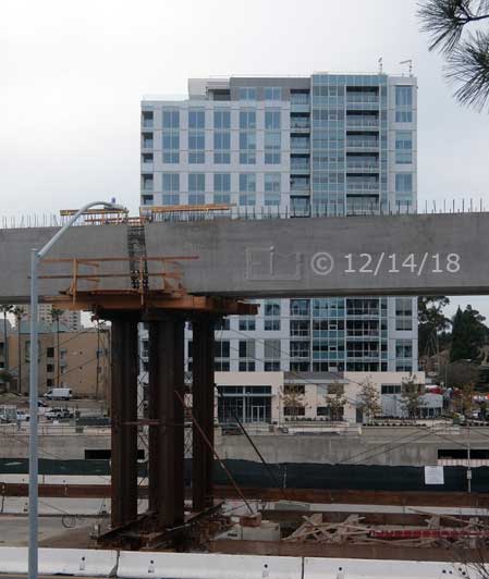 Color photo: New multistory building across Genesee Ave with trolley line construction in foreground - Embedded text: 12/14/18
