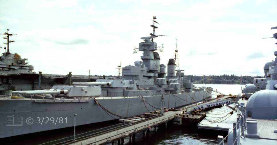 Color photo: Battleship New Jersey viewed across wharf from forward deck of Missouri - Embedded text: 3/29/81