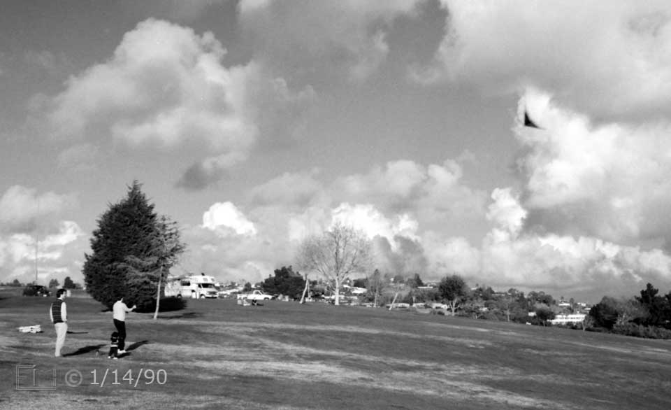 B/W photo: Kite flying in large, open area park - Embedded text: 1/14/90