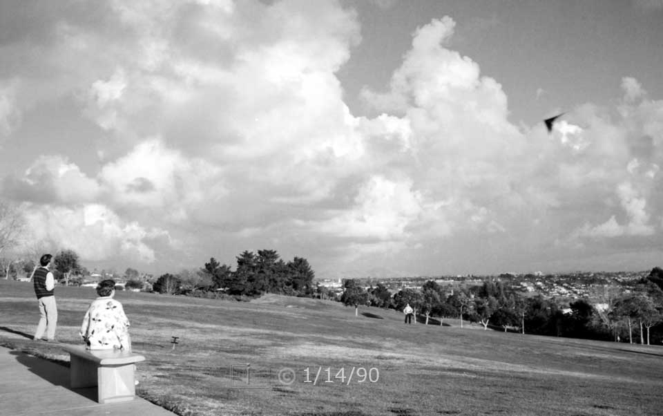 B/W photo: Kite flying in large, open area park - Embedded text: 1/14/90