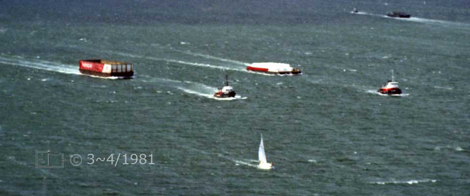 Color photo: Landscape view of a sailboat and 2 tugboats hauling barges - Embedded text: 3~4/1981
