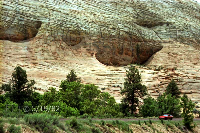Color photo: Red sportscar on highway in front of unique, rock formation, cliffside - Embedded text: 5/19/82