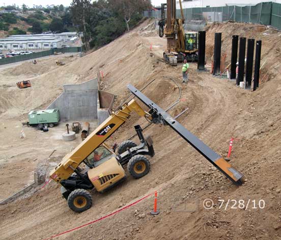 Color photo: Forklift truck transporting large I-beam up steep incline to top of hillside - Embedded text: 7/28/10
