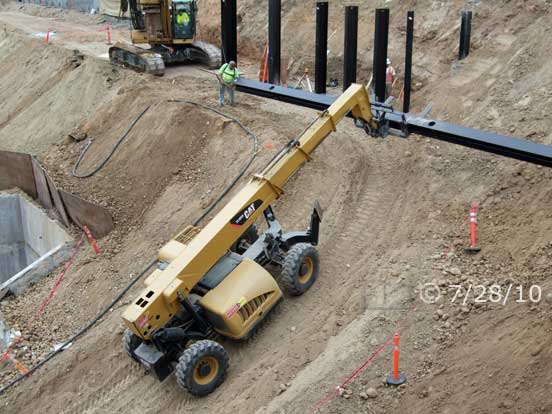 Color photo: Worker attaching cable from crane to end of I-beam - Embedded text: 7/28/10