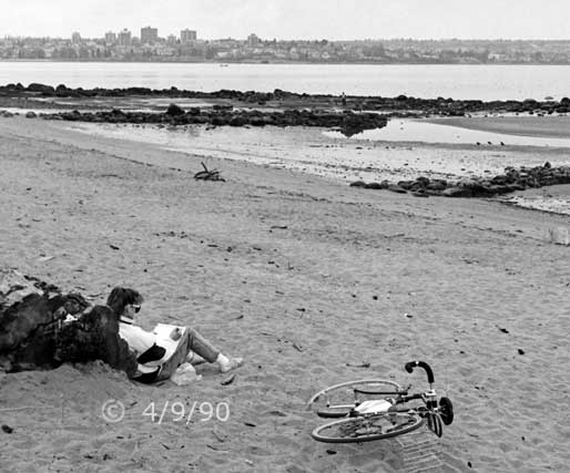B/W photo: Cyclist sitting on beach and drawing in a large sketch pad - Embedded text: 4/9/90