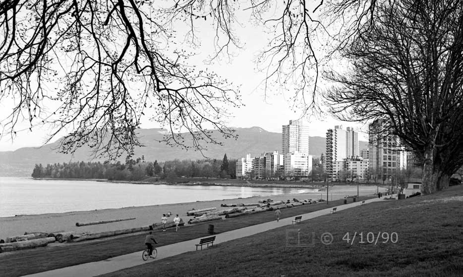 B/W photo: Walkway along Vancouver Beach with high-rises and Stanley Park in distance - Embedded text: 4/10/90