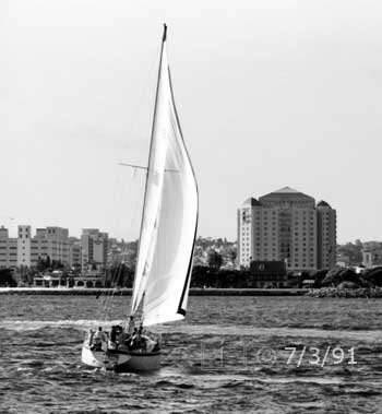 B/W photo: Stern view of boat under sail with San Diego skyline as background - Embedded text: 7/3/91