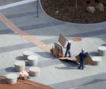 Color photo: Worker finishing wooden platform while protective cardboard cart away carpet is removed