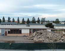 Color photo: Elevated view of remaining old West City building with rubble from demolished buildings slab piled in front