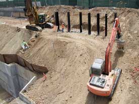 Color photo: Tracked excavator transporting loaded concrete bucket up steep incline to top of hillside
