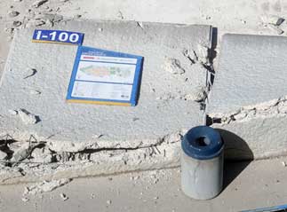 Color photo: View of remnant of collapsed wall w/ building ID and signage facing up