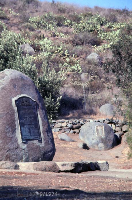 E6 Color image: Oblique view of monument with defunct (DARC) marker stone and boulder/cactus strewn hillside in background